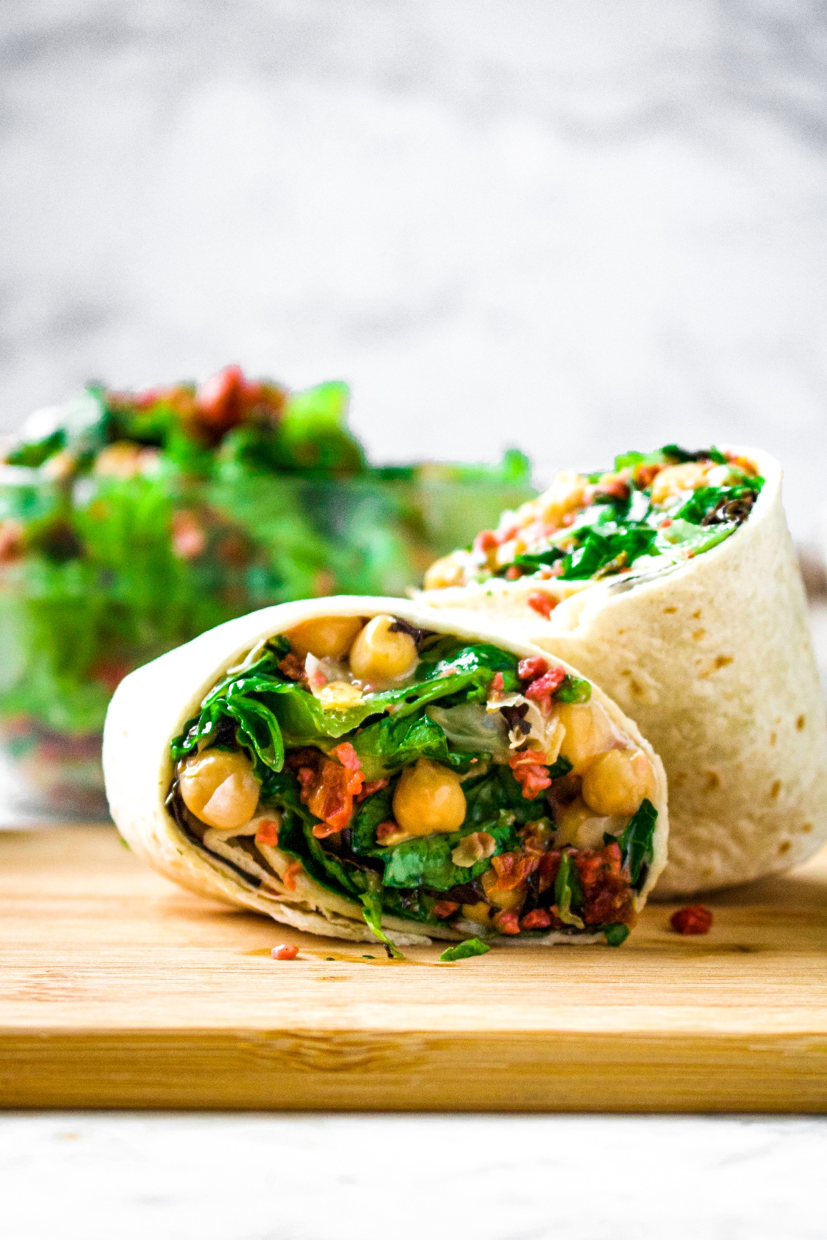 Head on shot of a sliced vegan chickpea bacon ranch wrap. There is a big green bowl of salad behind the wrap.
