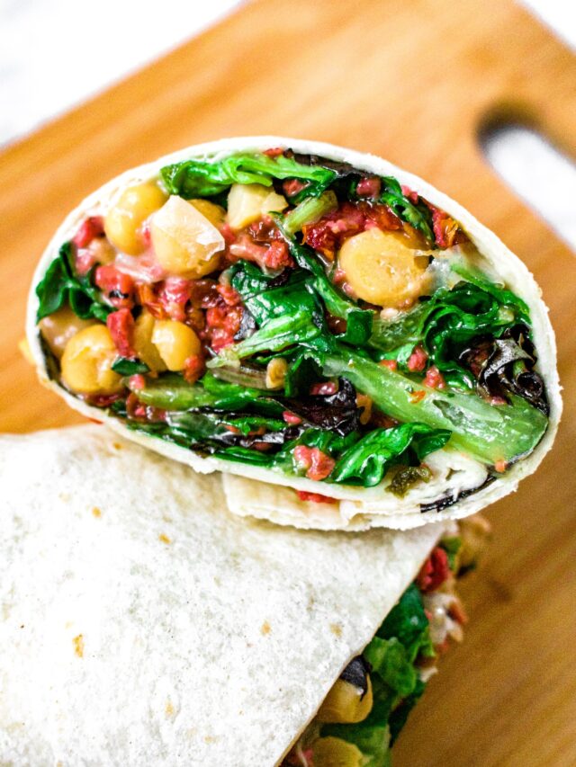 Overhead close up shot of a vegetarian and vegan wrap with chickpeas, dairy free ranch, greens, imitation bacon bits, and sun-dried tomatoes.