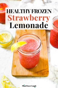 Overhead shot of a 12 oz mason jar full of strawberry lemonade smoothie. There is a lemon wedge on the glass, a bowl of lemon wedges behind it, and another glass of smoothie off to the side. Text reads: healthy frozen strawberry lemonade