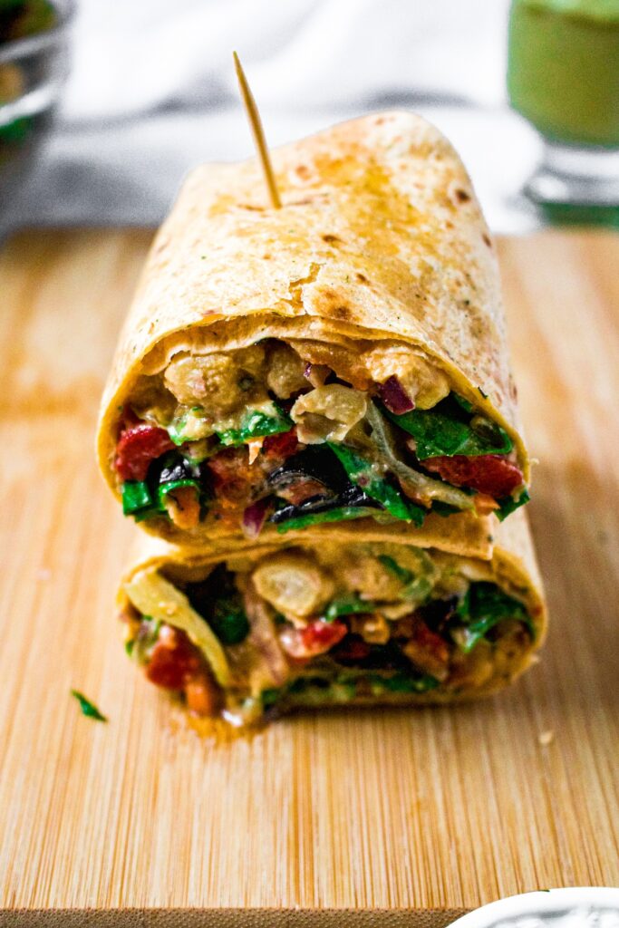 Head-on shot of a vegan mediterranean wrap cut into halves and stacked on top of each other, held together with a toothpick