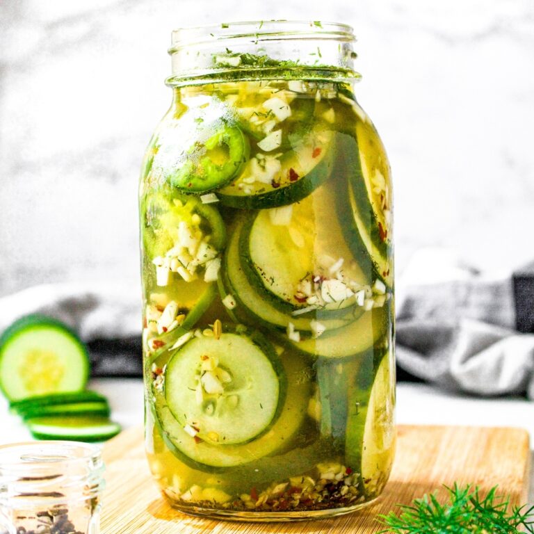 Head on view of a glass jar filled to the brim with sliced cucumbers and jalapenos in a no cook vinegar pickling brine.