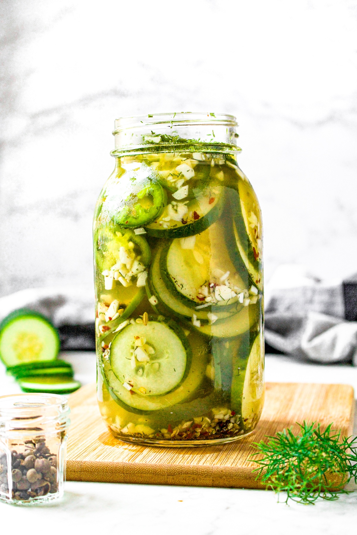 Head on shot of a glass jar filled to the brim with sliced cucumbers and jalapenos in a no cook vinegar pickling brine.