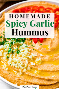 Overhead close up photo of a plate of spicy garlic hummus presented in a swirl pattern with olive oil drizzled into the crevices and topped with minced garlic, parsley, and sliced habanero peppers. Text reads: homemade spicy garlic hummus