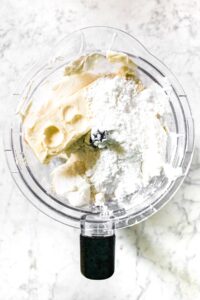 Overhead shot of a Ninja food processor with its lid off. It's filled with vegan butter, dairy free cream cheese, powdered sugar, lemon juice, refined coconut oil, and vanilla extract
