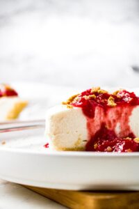 Head on shot of a slice of tofutti vegan cheesecake partially covered with strawberry sauce. There is another slice of dairy free cheesecake in the background.