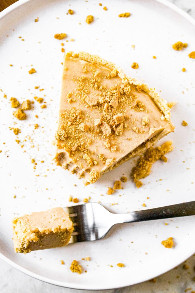 Overhead close up shot of a slice of peanut butter pie topped with vegan graham cracker crumbs. There is a bite taken out of the pie that resides on a fork sitting next to the slice.