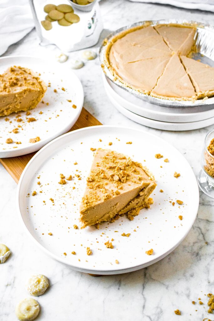 Overhead shot of 2 slices of vegan peanut butter pie on round white plates topped with graham cracker crumbs. There is a full pie sliced in the background.