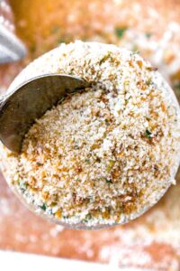 Overhead close up photo of an open jar of bread crumbs with a spoon going in.