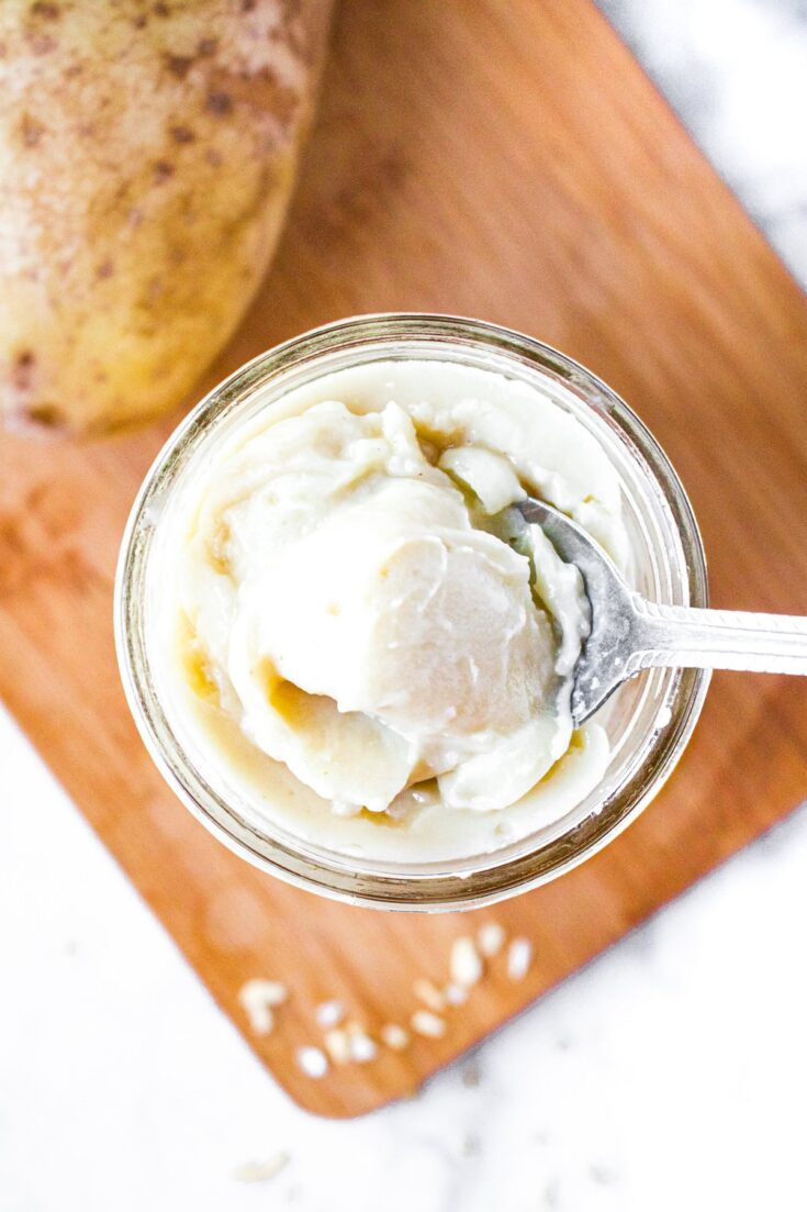 Overhead close up shot of an open glass jar of dairy free condensed potato soup with a spoon digging into it.