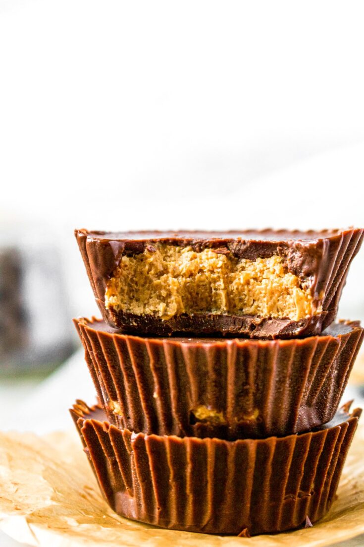 Close up head-on photo of a stack of 3 homemade peanut butter cups. There is a bite taken out of the top cup, exposing the peanut butter center!