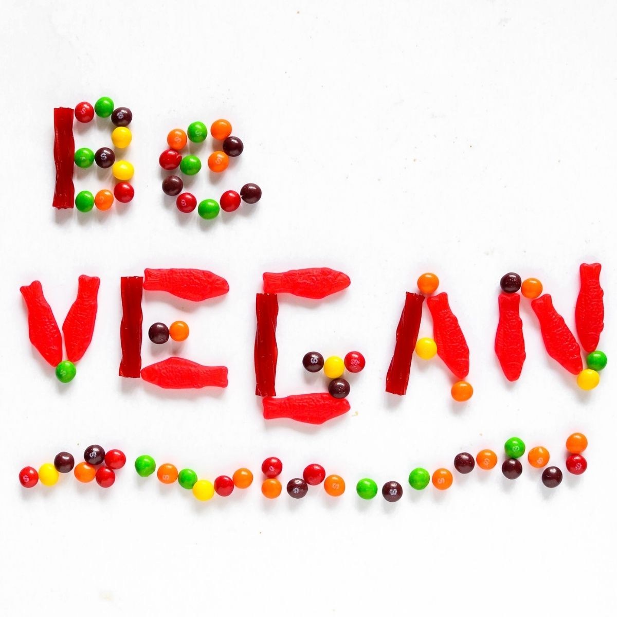 Overhead view of brightly colored gummy candy spelling out the words be vegan