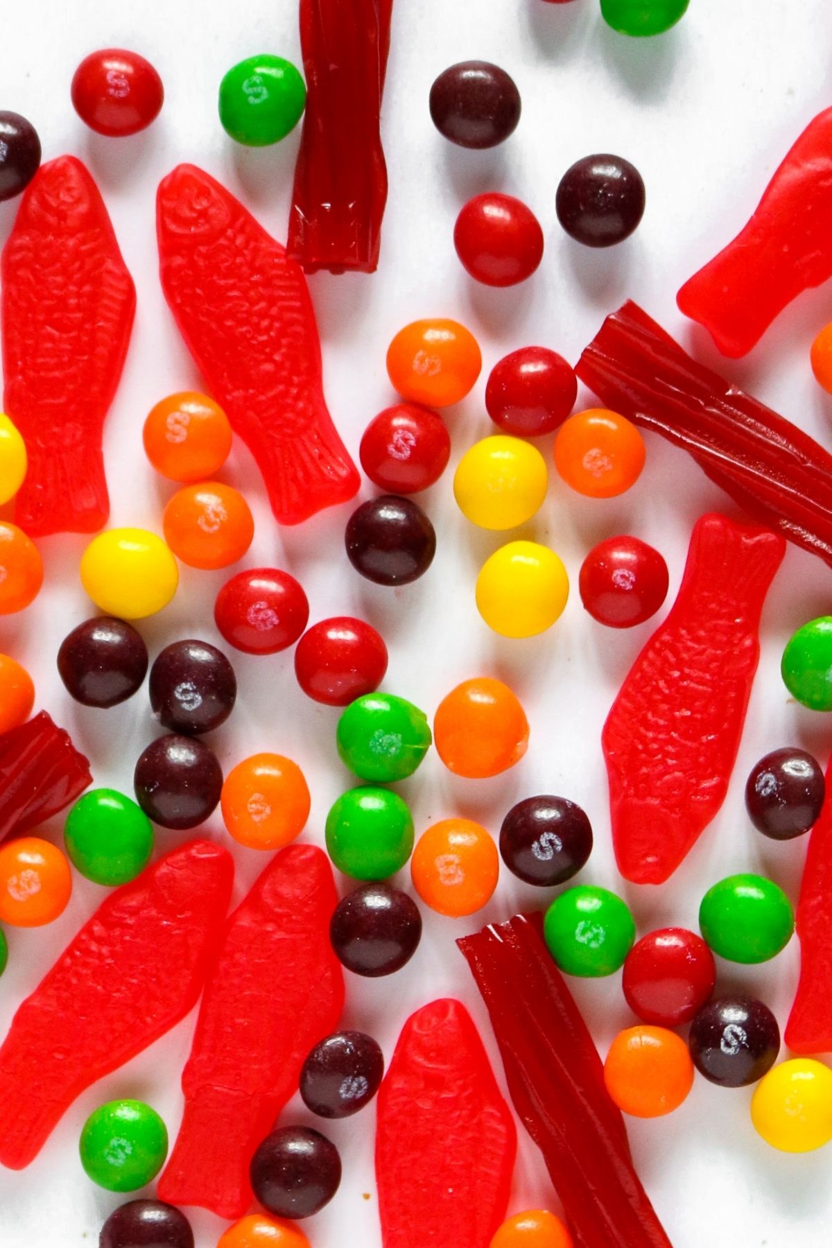 Overhead view of a pile of vegan candy like Fun Dip, Skittles, and Jolly Rancher Lollipops with a hand is reaching in to grab one of the lollipops.