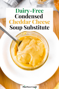 Overhead shot of a clear glass jar filled with vegan condensed cheese soup. There is a spoon digging into the soup to show the creamy thick texture. Text reads: dairy-free condensed cheddar cheese soup substitute.