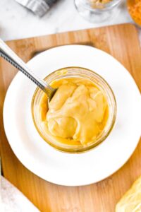 Overhead shot of a clear glass jar filled with vegan condensed cheese soup. There is a spoon digging into the soup to show the creamy thick texture.