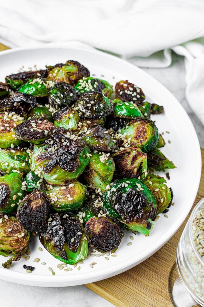 Overhead shot of a round white plate piled high with slightly charred sesame brussel sprouts sprinkled with sesame seeds
