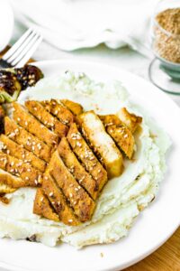 Overhead shot of two sliced tofu cutlets sitting on top of a pile of dairy-free mashed potatoes and sprinkled with sesame seeds