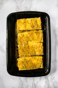 Overhead shot of a black rectangular container with marinating vegan lemon pepper chicken in it