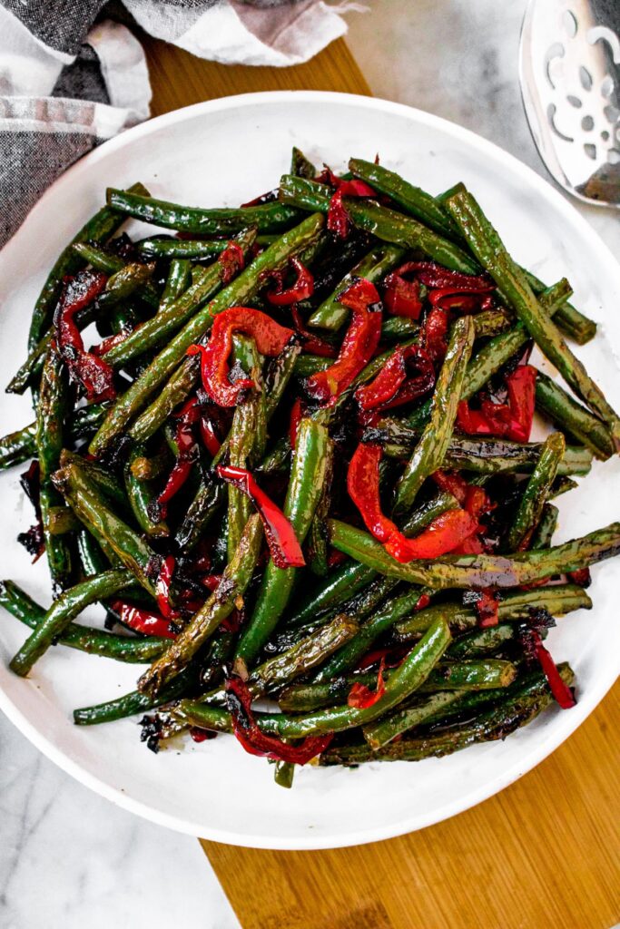 Overhead shot of a round white plate piled high with seared green beans and red peppers. There's a black and white checkered linen in the top left corner