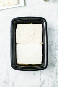 Two large squares of tofu in a black rectangular take-out container