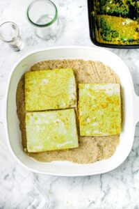 Overhead shot of 3 large squares of tofu on top of bread crumbs in a large square baking dish