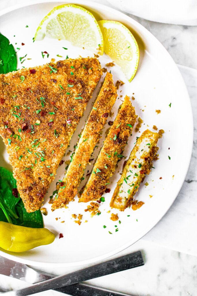 Close up overhead shot of a sliced crispy breaded tofu cutlet sprinkled with herbs and crushed red pepper