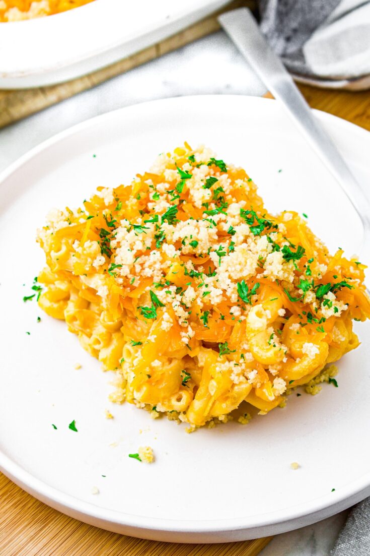 A square slice of vegan tofu mac and cheese on a plate sprinkled with minced herbs