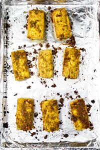 Overhead shot of eight baked tofu rectanglular slices on a foil-lined baking sheet