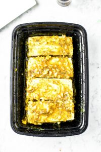 Overhead shot of a black rectangular container lined with marinated tofu slices