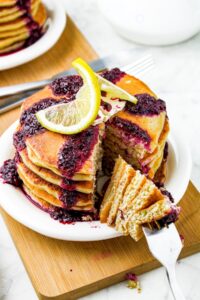 Head on photo of a stack of vegan pancakes with a triangle-shaped slice being taken out of them on a fork