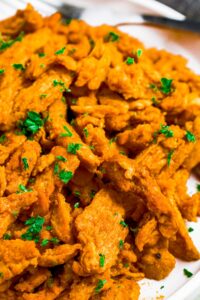 Close up shot of a pile of buffalo soy curls topped with minced green herbs