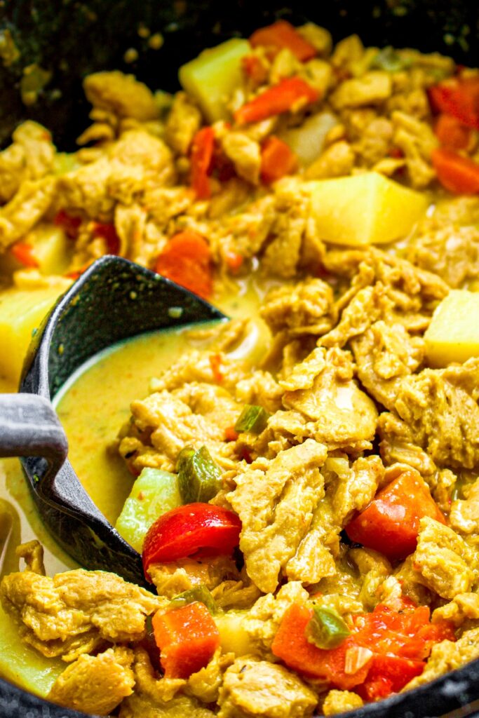 Close up overhead photo of a ladle digging into a slow cooker filled with vegan chicken curry