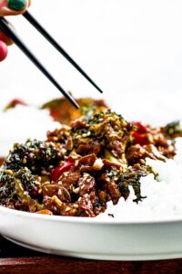 Head on photo of a pair of chopsticks reaching down to pick up a piece of vegan beef and broccoli