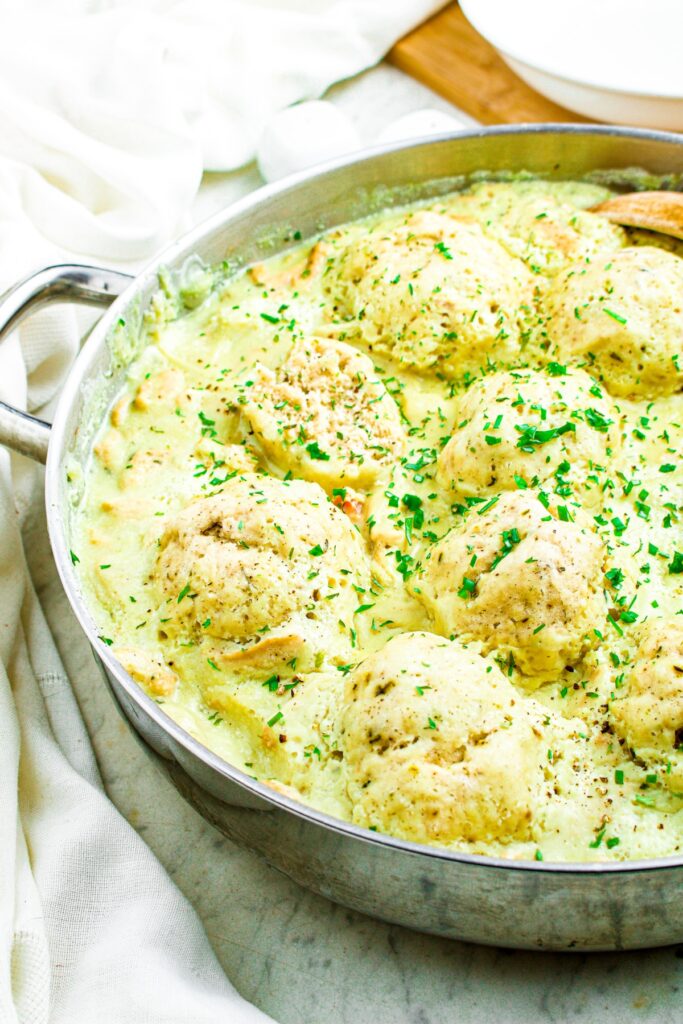 Overhead photo of a pan filled with vegan chicken and dumplings sprinkled with fresh green herbs