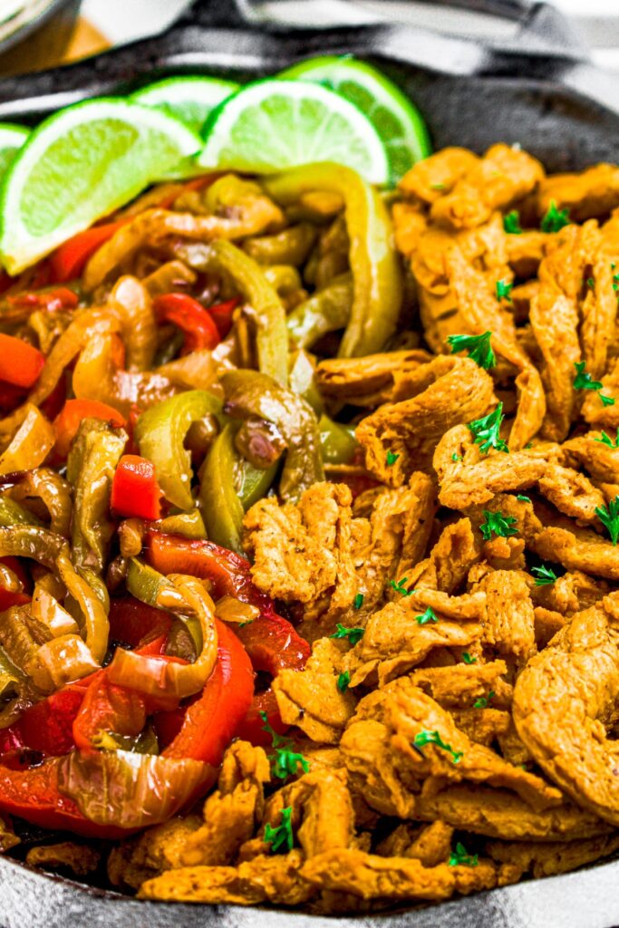 Close up overhead shot of a cast iron pan filled with soy curls, peppers and onions, and lime wedges
