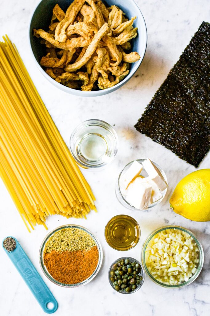 Overhead shot of all the ingredients you need to make vegan linguine clam sauce: linguine, nori, lemon, garlic, spices, vegan butter, white wine, soy sauce
