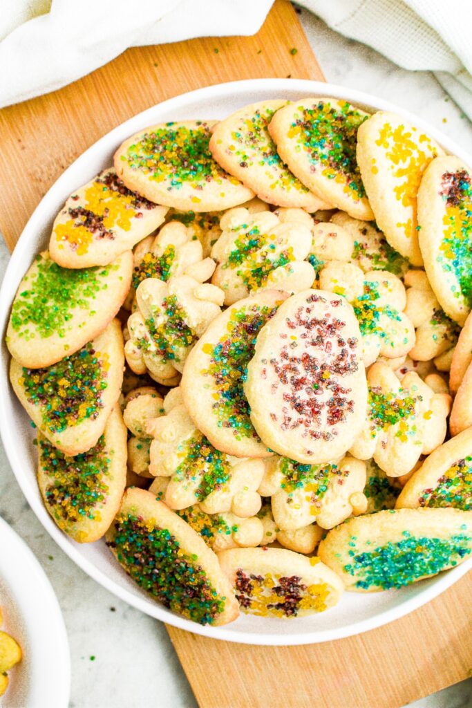 Overhead photo of a round white plate piled high with vegan spritz cookies decorated for Easter