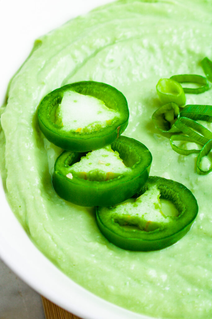 Close up overhead photo of a bowl of creamy avocado ranch sauce with sliced jalapenos on top
