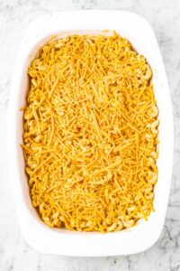 overhead photo of a white rectangular casserole dish with vegan mac and cheese covered in dairy-free cheese shreds