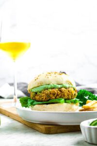 Head on photo of a california veggie burger on a plate with guac and lettuce with a white wine glass behind it