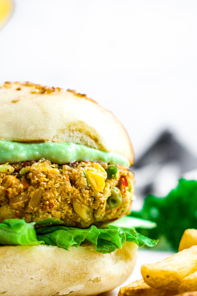 Close up head on photo of a veggie burger on a bun with creamy guacamole and lettuce