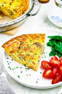 Head on photo of a slice of just egg quiche on a plate with sauteed spinach and tomatoes