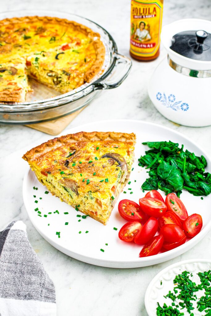 Overhead photo of a slice of just egg quiche on a plate with spinach and sliced grape tomatoes