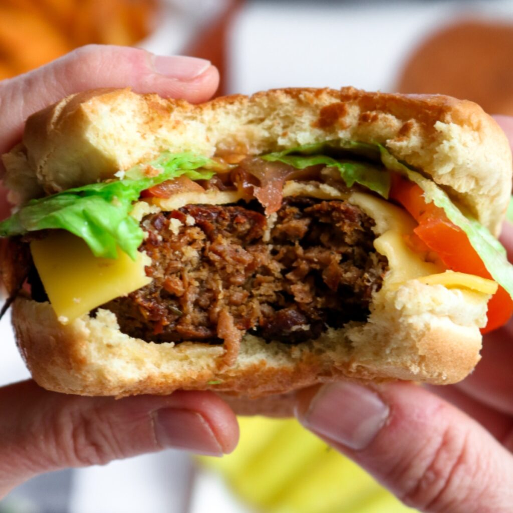 Close up overhead view of two hands holding a vegan cheeseburger with lettuce and tomato with a big bite taken out of the center