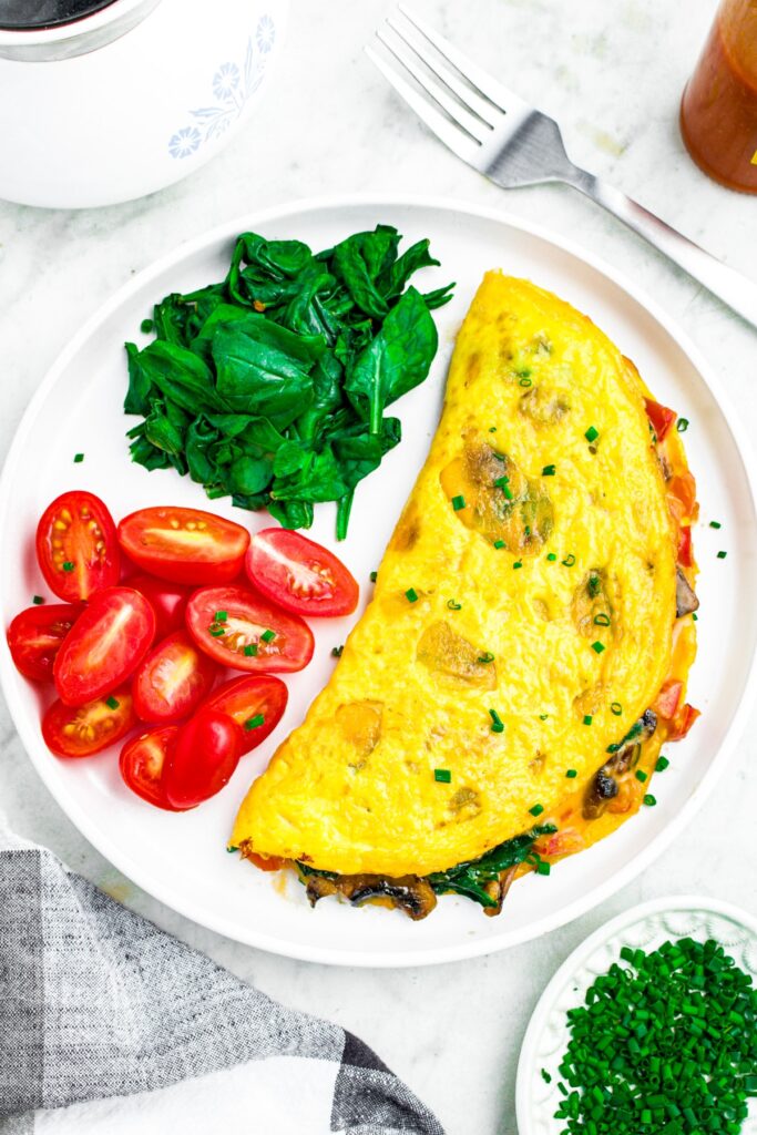 Overhead photo of a round white plate with a vegan omelette on one side and cherry tomatoes / sauteed spinach on the other side