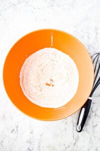 Overhead photo of a large mixing bowl with flour and other dry ingredients mixed with a whisk that sits to the right of the bowl