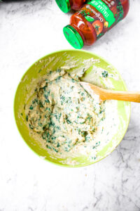 Overhead photo of a large mixing bowl with a spoon mixing tofu ricotta and spinach together