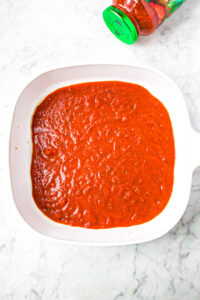 Overhead photo of a square baking dish with a thin layer of tomato sauce on the bottom