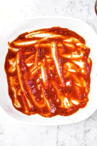 Overhead photo of a layer of marinara sauce in the bottom of a square baking dish