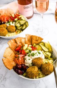 Overhead photo of a bowl of falafel balls with kalamata olives, crispy pita, pickles, and a vegan feta sauce