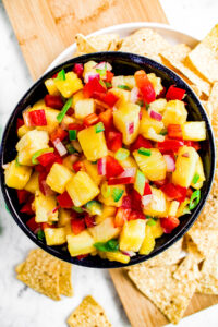 Overhead zoomed in photo of a small bowl of sesame pineapple jalapeno salsa surrounded by triangular tortilla chips